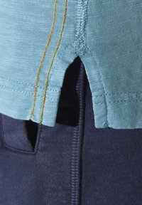 Light blue short-sleeve shirt featuring a textured fabric, split hem, and contrasting yellow stitching, paired with dark navy pants with pockets.