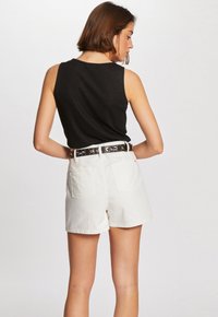 Black sleeveless top paired with high-waisted white shorts. The shorts have back pockets and a patterned belt with a dark background and colorful design.
