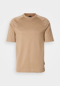 Bež majica s kratkimi rokavi in okroglim izrezom, izdelana iz mehke tkanine. Ima raglan rokave in majhno logotipno nalepko na strani.