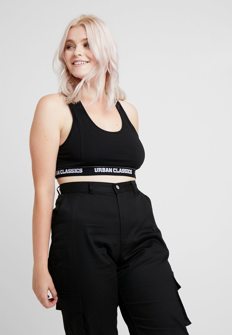 Svart croppad tanktopp med racerback-design och vit "URBAN CLASSICS" logoband. Kombinerad med högmidjade svarta cargobyxor.