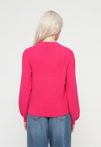 Fuksijas džemperis ar puffa garajām piedurknēm un ribotām malām. Izgatavots no mīksta materiāla, tai ir apaļa kakla izgriezuma un gluda tekstūra.