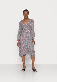 Vestido midi floral com fundo preto, apresentando flores rosas e azuis, mangas longas, decote em V e um裾 plissado. Sapatos de salto aberto pretos.