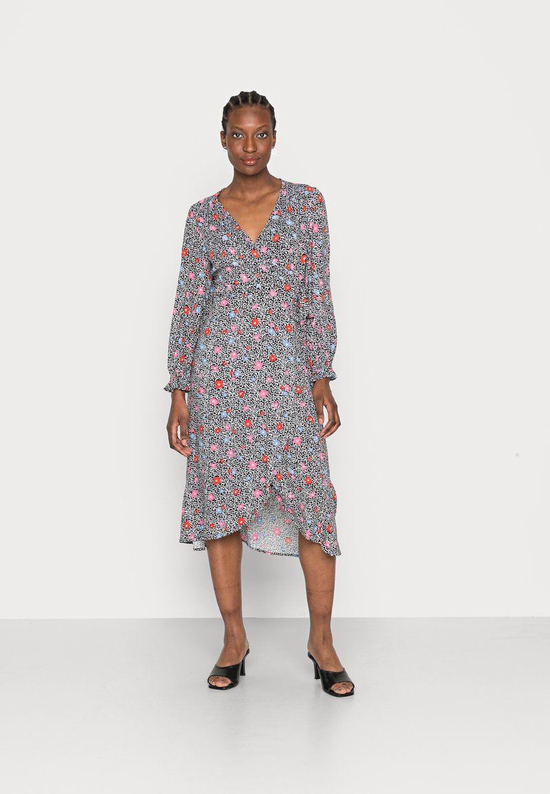 Vestido midi floral com fundo preto, apresentando flores rosas e azuis, mangas longas, decote em V e um裾 plissado. Sapatos de salto aberto pretos.