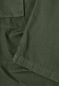 Tessuto verde oliva con una trama fine e texturizzata. Presenta un bordo dritto e una cucitura dettagliata lungo l'orlo.