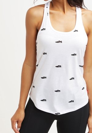 Biały top na ramiączkach z małymi czarnymi nadrukami w kształcie tenisówek, wykonany z miękkiej tkaniny, z okrągłym dekoltem i tyłem na ramiączkach w stylu racerback, posiadający zaokrąglony dół.