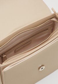 Beige axelväska med en strukturerad design, med dragkedjor i guld och en tryckknapp. Insidan har flera fack.