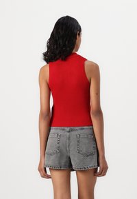 Rød ribbet ermeløs topp med høy krage, kombinert med høyt liv grå denim shorts, som viser ryggdetaljer og teksturert stoff.