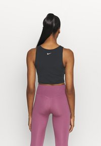 Débardeur noir court en tissu lisse, avec un petit logo blanc au dos, assorti à un legging violet taille haute.