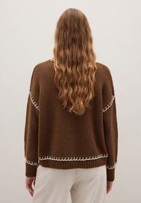 Brauner gestrickter Pullover mit lockerer Passform, mit weißen dekorativen Nähten entlang der Nähte. Strukturierter Stoff und gerippte Bündchen.