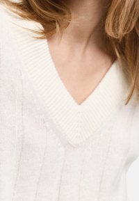 Pull blanc en maille avec une texture côtelée et un col en V. Présente de fines lignes verticales et un tissu doux et léger.