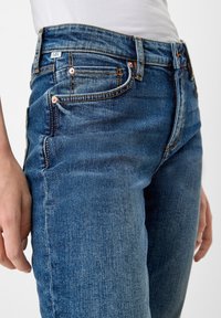 Dark blue denim jeans with a fitted design, five pockets, visible stitching, and copper-tone hardware. Smooth texture with slight distressing.