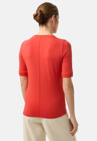 Czerwona dopasowana koszulka z krótkimi rękawami i okrągłym dekoltem. Wykonana z gładkiego materiału, posiada szew wzdłuż środka pleców.