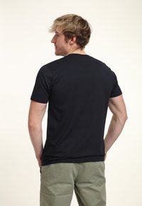 Black short-sleeve t-shirt in a smooth fabric, featuring a classic crew neck design. Worn with olive green pants, showing a relaxed fit.