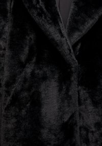 Haină neagră din blană artificială, cu un guler pliat, evidențiind textura moale și densă și o cusătură de-a lungul deschiderii frontale.