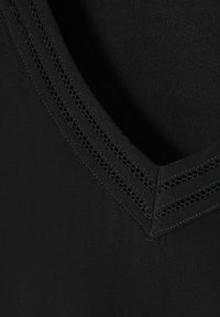 Haut en tissu noir avec un design à col en V, présentant des coutures texturées et une finition lisse. L'encolure possède un motif de bordure détaillé.