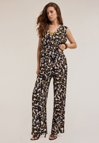 Tuta con fantasia floreale, scollatura a V profonda, vita fasciata, gambe ampie e una combinazione di colori verde, blu navy e crema; tessuto leggero.