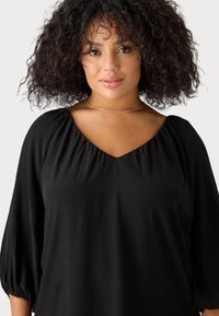 Blusa nera con scollatura a V, maniche a sbuffo e tessuto morbido con una leggera trama. Il design è di vestibilità comoda e leggera.