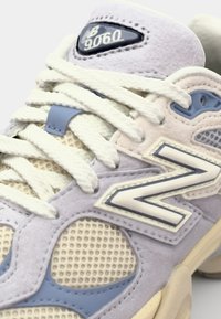 New Balance 9060 sneakers feature a light purple and cream suede design, mesh panels, flat white laces, and a blue logo accent.