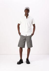 White short-sleeve button-up shirt; gray cargo shorts with pockets; black chunky-soled shoes; gray cap with embellishments.