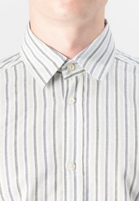 Camicia a righe grigia chiara, caratterizzata da sottili righe verticali in nero e blu navy. Texture morbida con colletto classico e due bottoni.