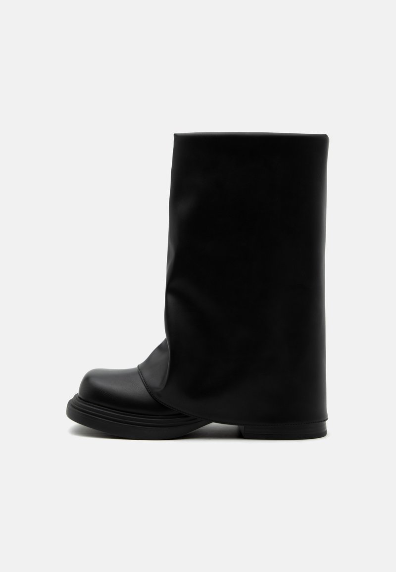 Botte haute en cuir noir avec une tige supérieure large et ample et une semelle épaisse et arrondie sur fond blanc.