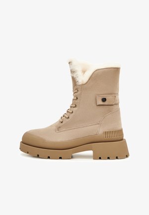 Botine bej cu o căptușeală moale din blană sintetică, talpă robustă din cauciuc și sistem de închidere cu șireturi. Prezintă un detaliu cu un buton pe lateral și vârf întărit.