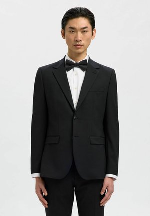 Mustast smokingujakist, millel on kaks eesmist taskut, sälkadega krae ja ühe nupuga kinnis, kombineerituna valge särgi ja musta kikilipsuga.