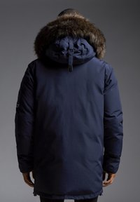 Marinblå parka med en fuskpäls-fodrad huva, dragkedjestängning och sidofickor, designad för värme och utomhusbruk.