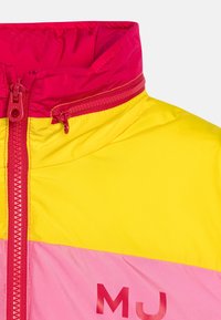 Färgglad, lätt jacka med dragkedja fram, hög krage och färgblockdesign i rosa, gult och röda accenter.