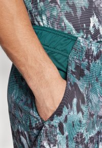 Un tissu léger et à motifs présente des nuances de vert et de noir avec des textures en grille. Comprend une poche latérale avec une bordure verte unie.