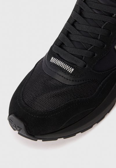 Baskets de sport noires avec un mélange de matériaux en maille et en daim, bout rond, lacets noirs et semelle en caoutchouc texturée.