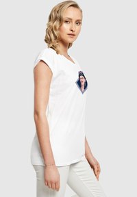 Hvid bomulds T-shirt med korte ærmer, der har et farverigt grafisk motiv af en kvindes ansigt i en diamantform på fronten.