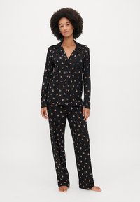 Set de pijamale negre dintr-un material moale, cu un model floral în nuanțe de roz și verde. Top cu mâneci lungi și nasturi, având un buzunar pe piept, și pantaloni asortati.