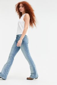 Heledad sinine laiade säärtega teksad, keskmise pesuga, denimitekstuuriga ja kerge venivusega, koos valge ilma varrukateta topiga.