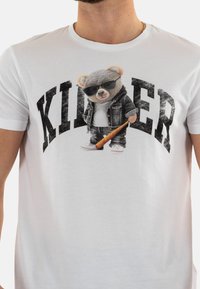 T-shirt en coton blanc avec une illustration d'un ours en peluche portant des lunettes de soleil et en tenue en denim, avec le mot "KILLER" en lettres noires en gras et usées.
