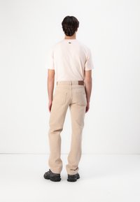 Camiseta de manga corta en rosa claro combinada con pantalones de algodón beige. Presenta un logo sutil en la parte trasera de la camiseta, con prácticos bolsillos traseros.