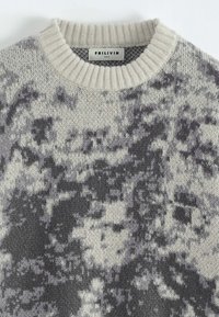 Pull en tricot avec un col rond, présentant un motif abstrait gris et blanc cassé, une texture douce et des détails côtelés au niveau du col. Étiquette de marque visible.
