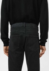 Vaqueros negros de mezclilla con un diseño ajustado, corte recto, dos bolsillos traseros y una cintura texturizada.