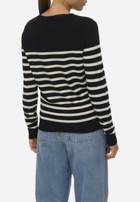 Maglione a righe blu navy e crema con maniche lunghe e collo rotondo, con orlo e polsini a costine. Indossato con jeans azzurri chiari.