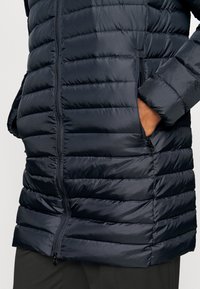 Mörk marinblå pufferjacka med horisontell quiltad design, med en framdragkedja och sidofickor, tillverkad av ett mjukt och lätt material.