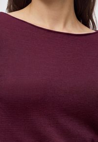 Gros plan d'une personne portant un haut côtelé ajusté de couleur violet foncé avec un col bateau, montrant la partie supérieure de la poitrine et du cou.