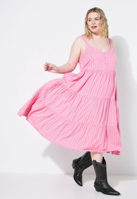 Růžové pruhované maxi šaty s patrovým designem, zdobené zapínáním na knoflíky vpředu, tenkými ramínky a volným střihem; doplněné černými botami se hroty.