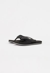 Svarte flip-flops med en teksturert overdel, som har to stropper og en hvit såleomriss. Laget av gummi, designet for komfort.