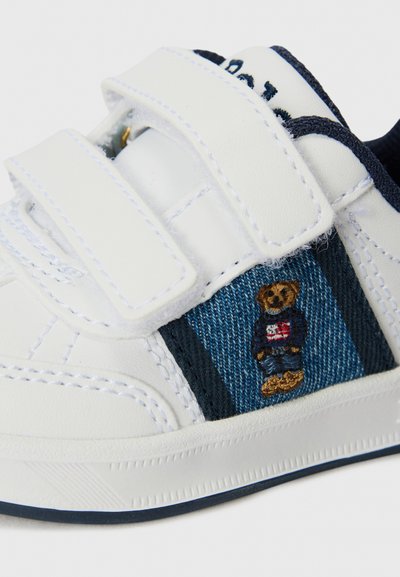 Hvite sneakers med to borrelåser, denimdetaljer og et brodert bjørnedesign. Har en teksturert såle og kontrasterende sting.