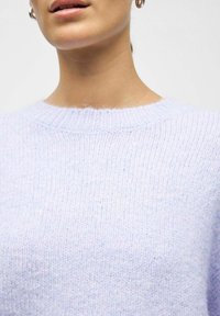 Jasnofioletowy dziany sweter z prążkowanym dekoltem i miękką fakturą, o luźnym kroju i minimalnie widocznych detalach szwów.