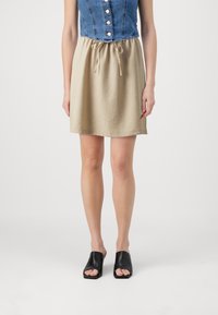 Haut en denim court avec des boutons, jupe beige à cordon de serrage et sandales noires ouvertes. Textures douces ; design décontracté.
