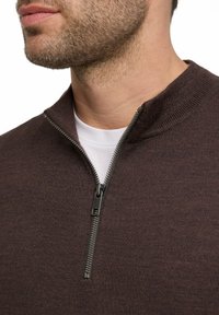 Maglione marrone con zip al collo realizzato in tessuto texturizzato, caratterizzato da una vestibilità slim e da una zip nera a contrasto. Indossato sopra una maglietta bianca.