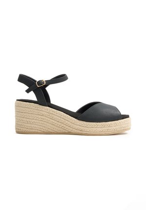 Sandalia de cuña negra con pulsera en el tobillo, puntera abierta y suela de esparto trenzada beige.