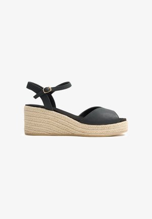 Sandalia de cuña negra con pulsera en el tobillo, puntera abierta y suela de esparto trenzada beige.