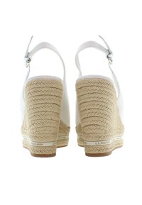 Bílé espadrilky na wedge podpatcích s pletenou jute patou, nastavitelným páskem a značkovým akcentem na podrážce. Hladký povrch a robustní design.